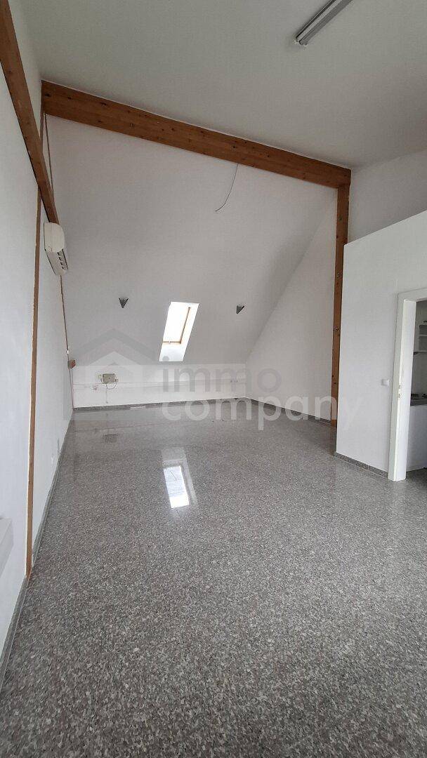 Geräumiger, leerer Raum mit Dachschrägen, Holzbalken und einem Dachfenster, ideal für verschiedene Nutzungen.