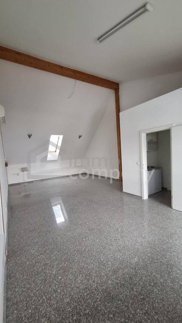 Offener Gewerberaum mit Dachschrägen, Holzbalken und einem Dachfenster, ideal für flexible Nutzungsmöglichkeiten.