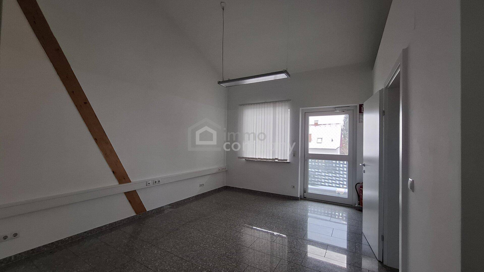 Heller Büroraum im Dachgeschoss mit Fliesenboden, Fenster und Tür, die viel Tageslicht hereinlassen.