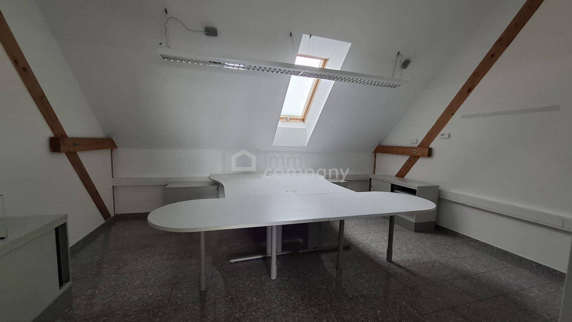 Dachgeschossbüro mit großem Schreibtisch, Dachfenstern und sichtbaren Holzbalken, ideal für kreatives Arbeiten.