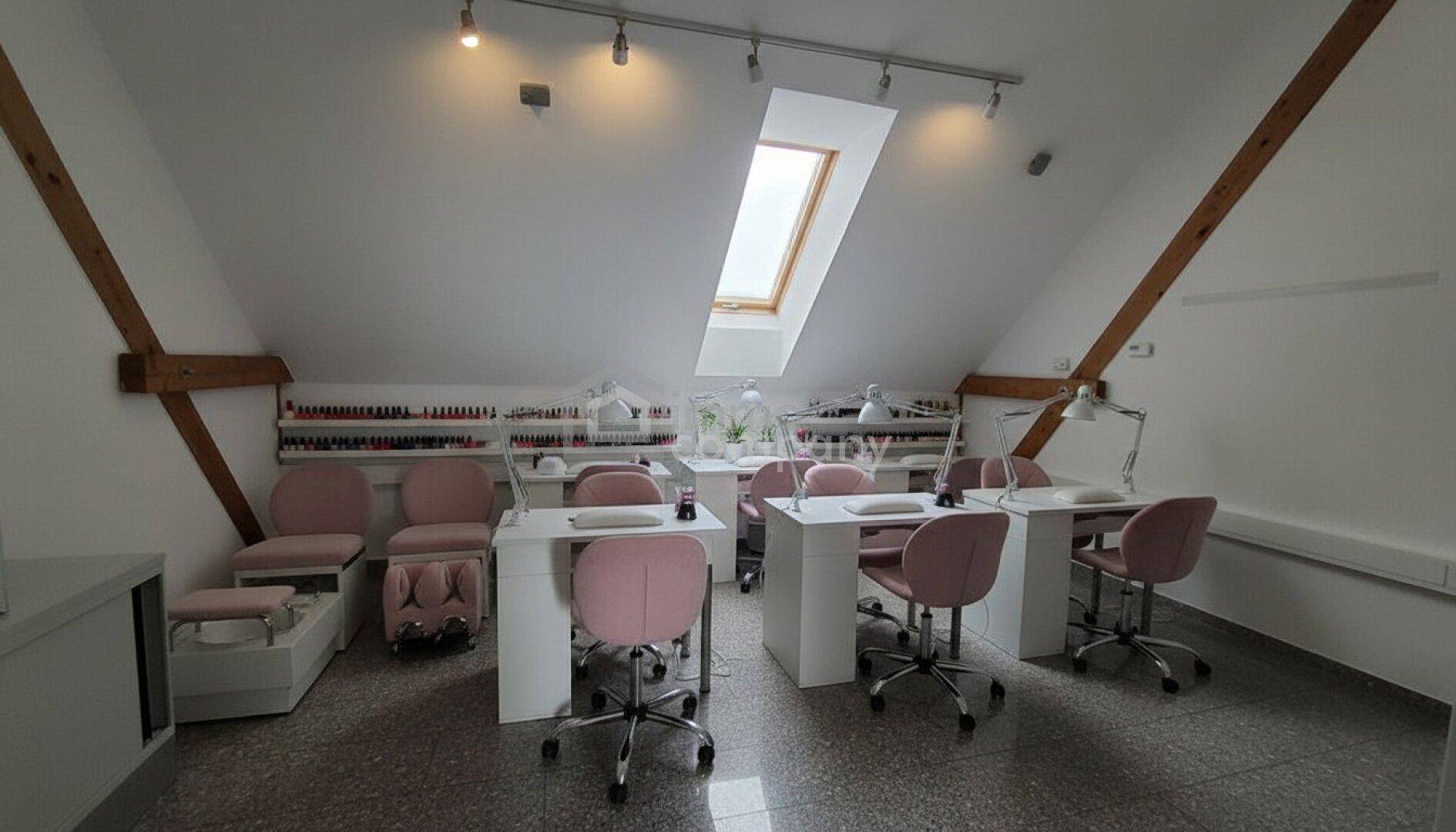 Heller Nagelstudio-Raum im Dachgeschoss mit mehreren Arbeitsplätzen, rosa Stühlen und Dachfenstern.