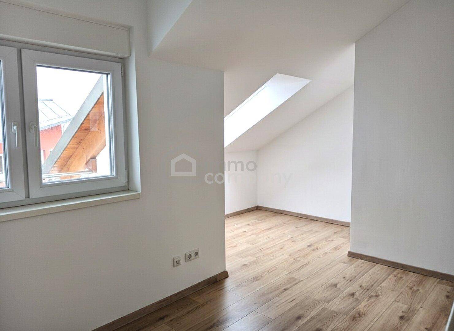 Helles Zimmer im Dachgeschoss mit Dachschräge, Laminatboden und Dachfenster für natürliches Licht.