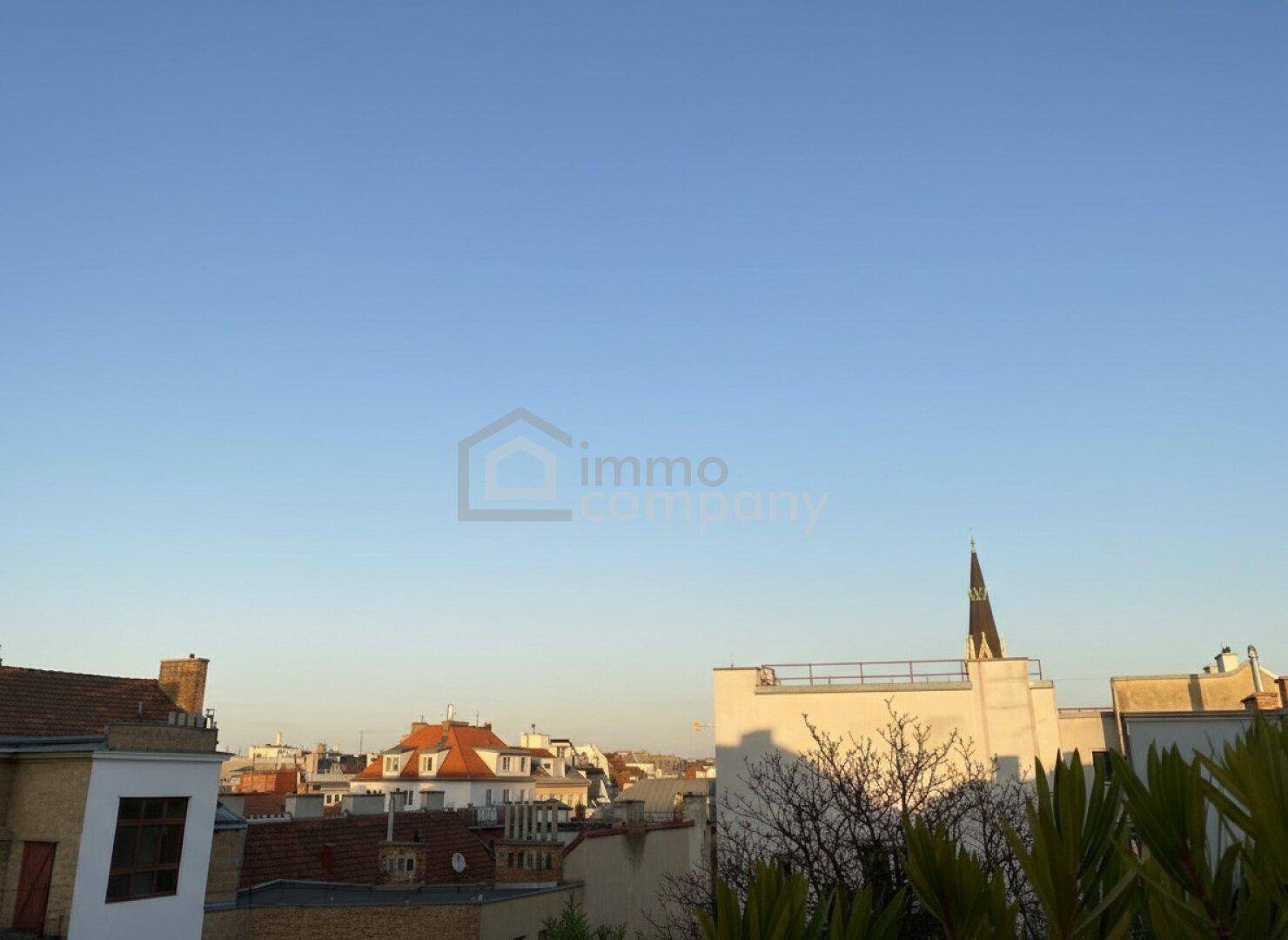 Weitläufiger Blick über die Stadt bei Sonnenuntergang mit verschiedenen Dächern und Gebäuden.