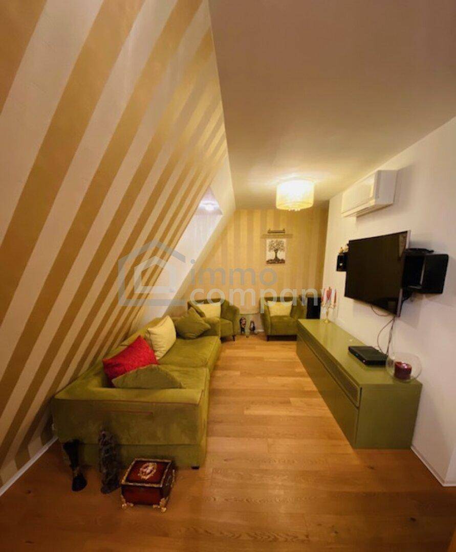 Gemütliches Wohnzimmer mit schrägen Wänden, Holzboden und einem grünen Ecksofa.