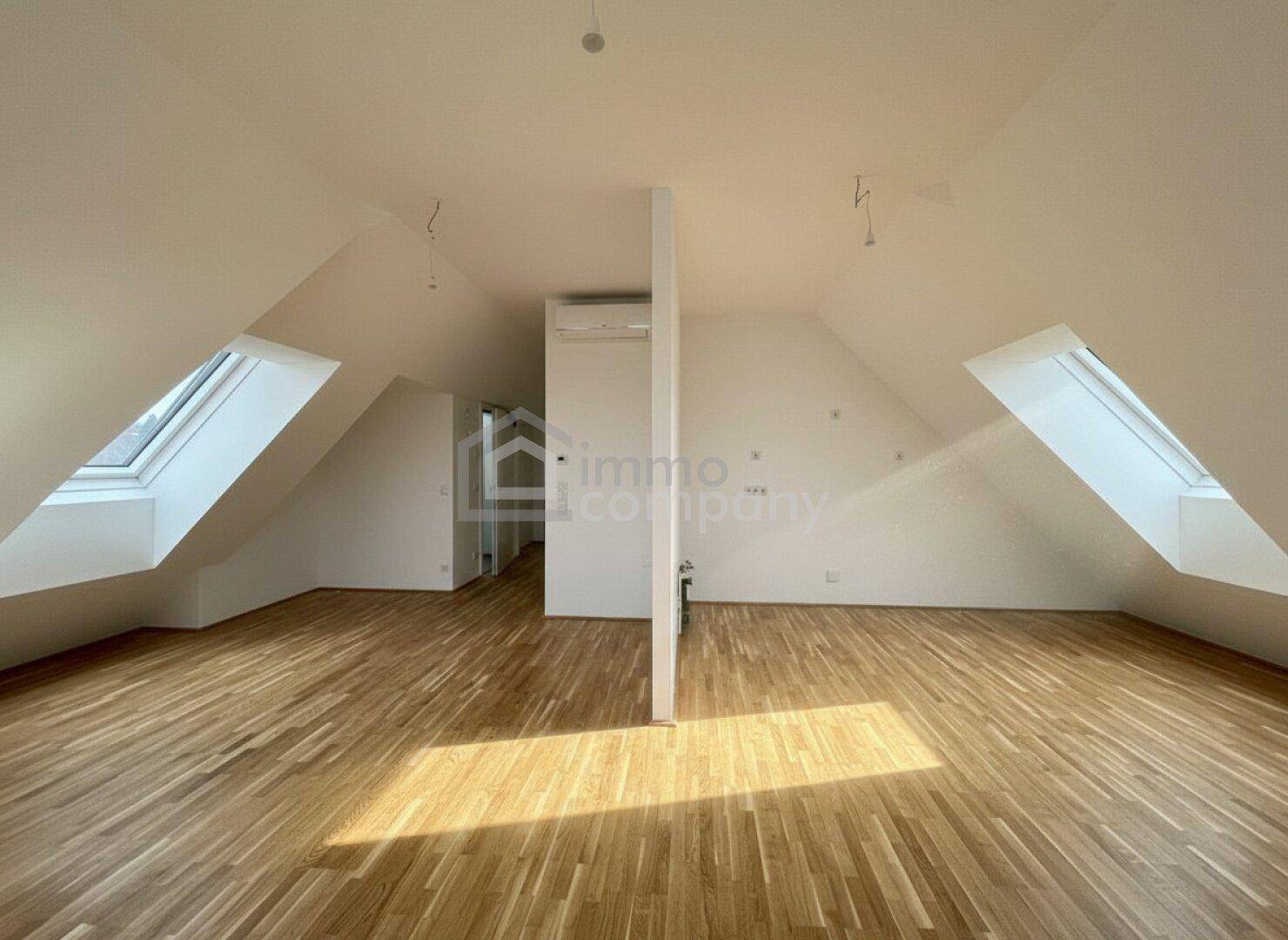 Heller, unmöblierter Dachgeschossraum mit Holzboden und mehreren Dachfenstern.