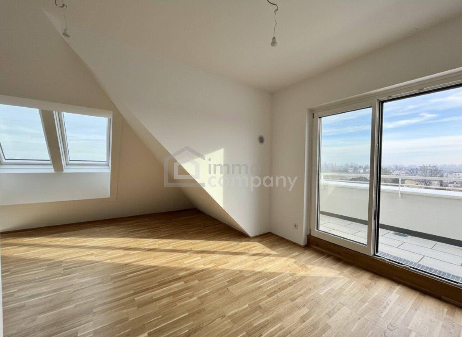 Geräumiger, unmöblierter Raum mit Holzboden, Dachfenstern und großem Terrassenzugang.