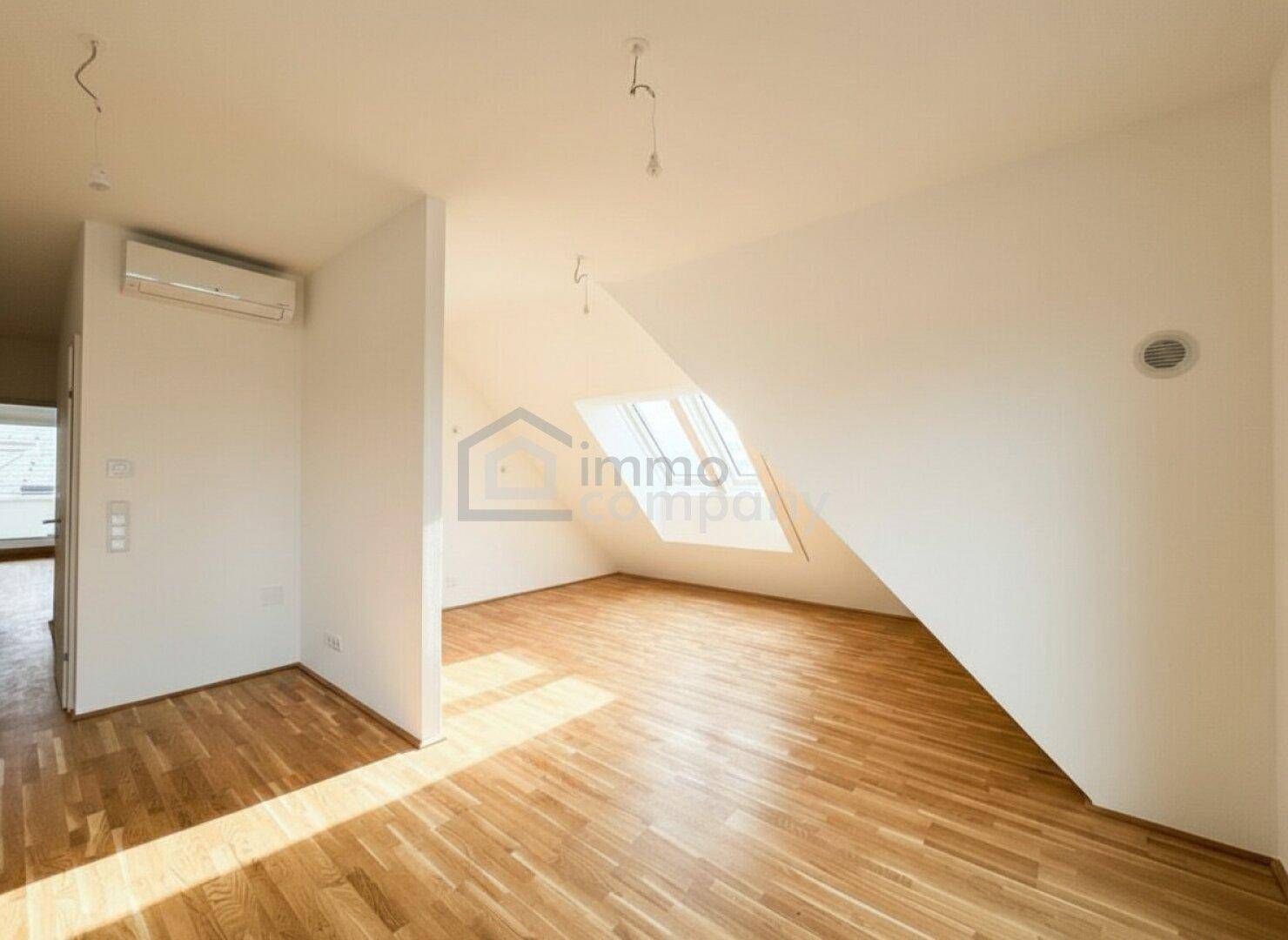 Geräumiger, unmöblierter Raum im Dachgeschoss mit Holzboden und Dachfenster.