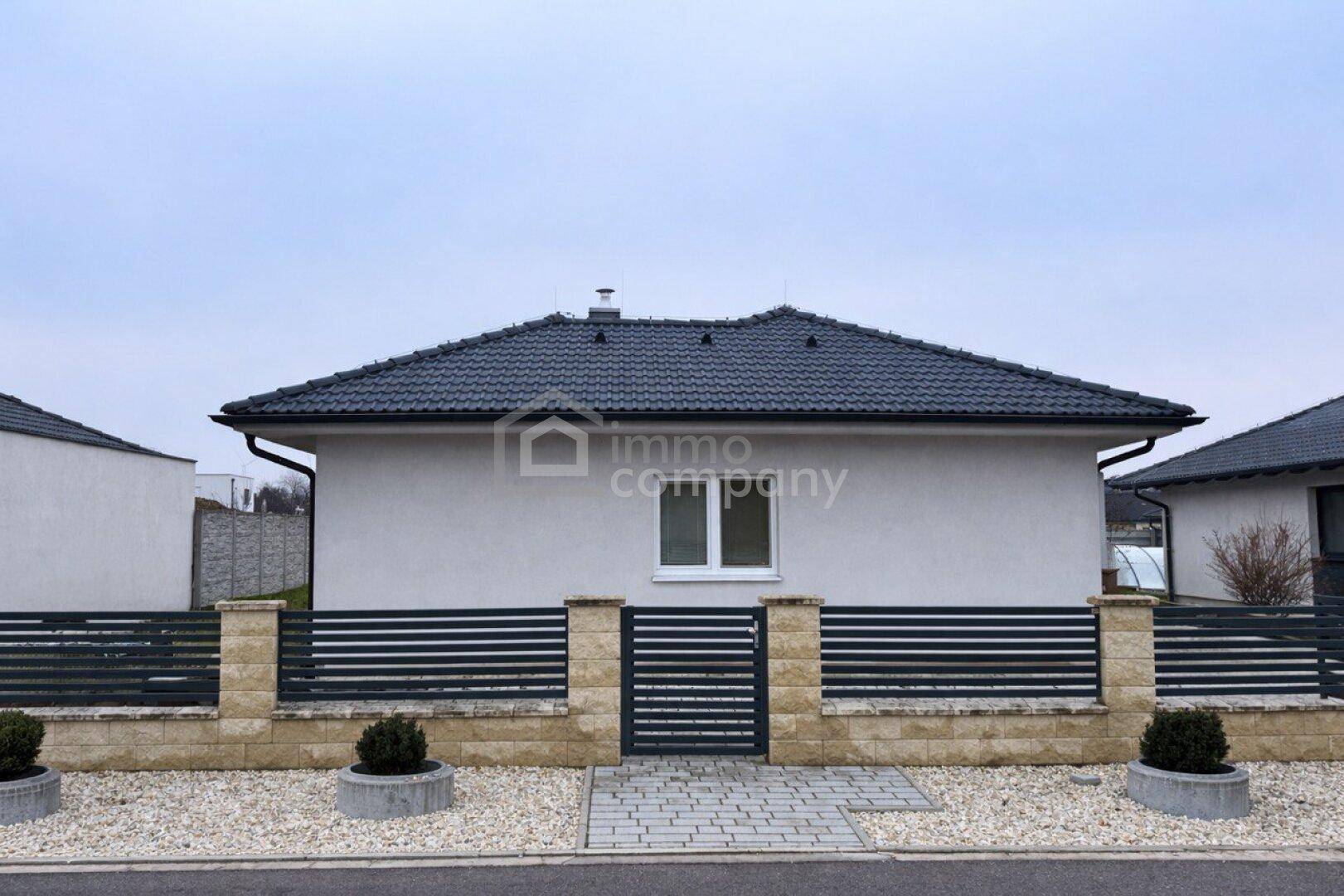 Vorderansicht eines modernen Einfamilienhauses mit dunklem Dach und gepflegtem Vorgarten.