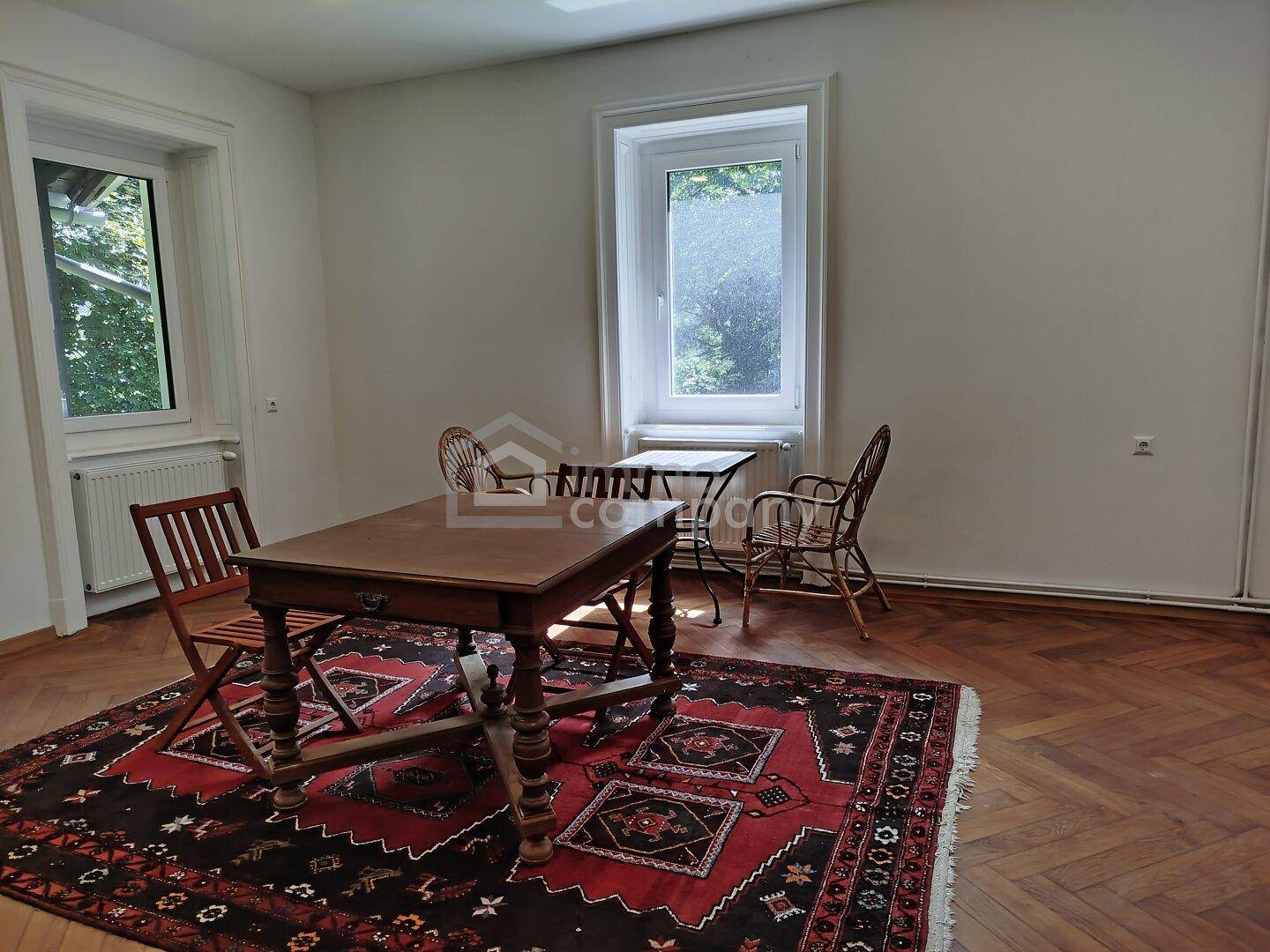 Geräumiger Essbereich mit traditionellem Teppich, Holztisch und zwei großen Fenstern mit Ausblick.
