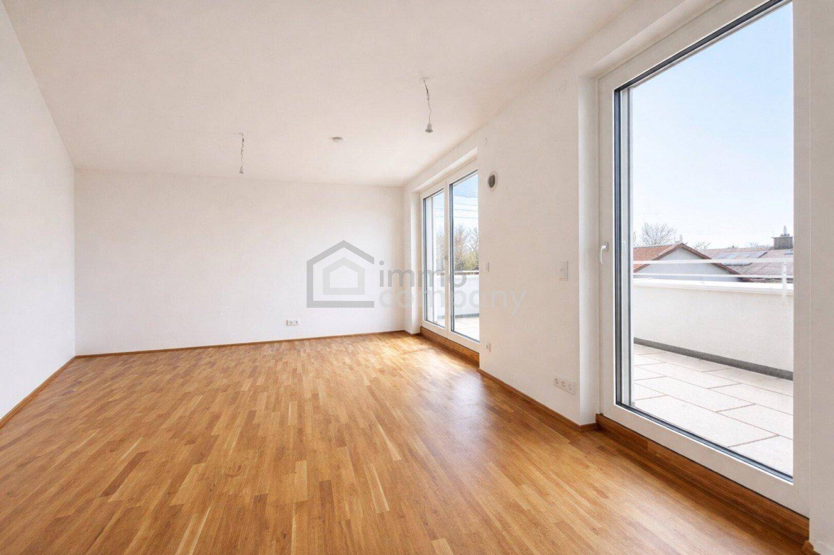 Geräumiger Wohnbereich mit hellem Parkettboden und Zugang zu einer sonnigen Terrasse.