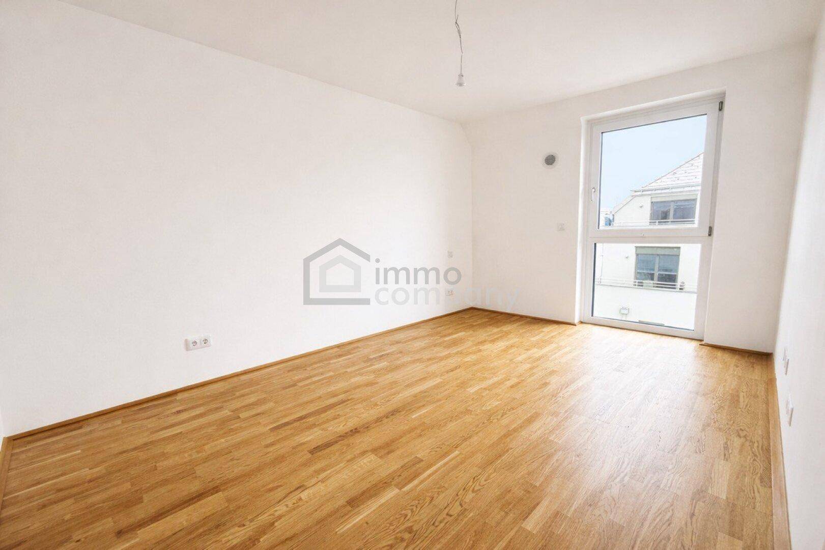 Helles, leeres Zimmer mit Parkettboden und großem Fenster, ideal als Schlafzimmer.