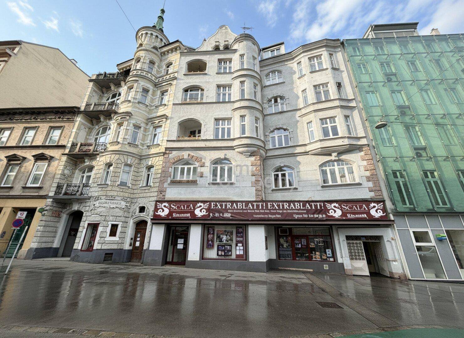 Historisches Gebäude mit reich verzierter Fassade und Geschäften im Erdgeschoss.