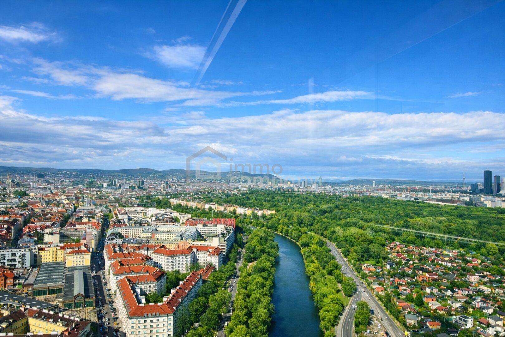 Panoramablick über die Stadt mit Fluss, grünen Parks und Wohngebäuden unter blauem Himmel.