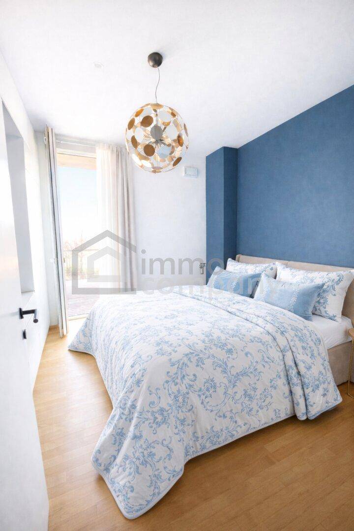 Helles Schlafzimmer mit blauer Akzentwand, Holzboden und Zugang zum Balkon.