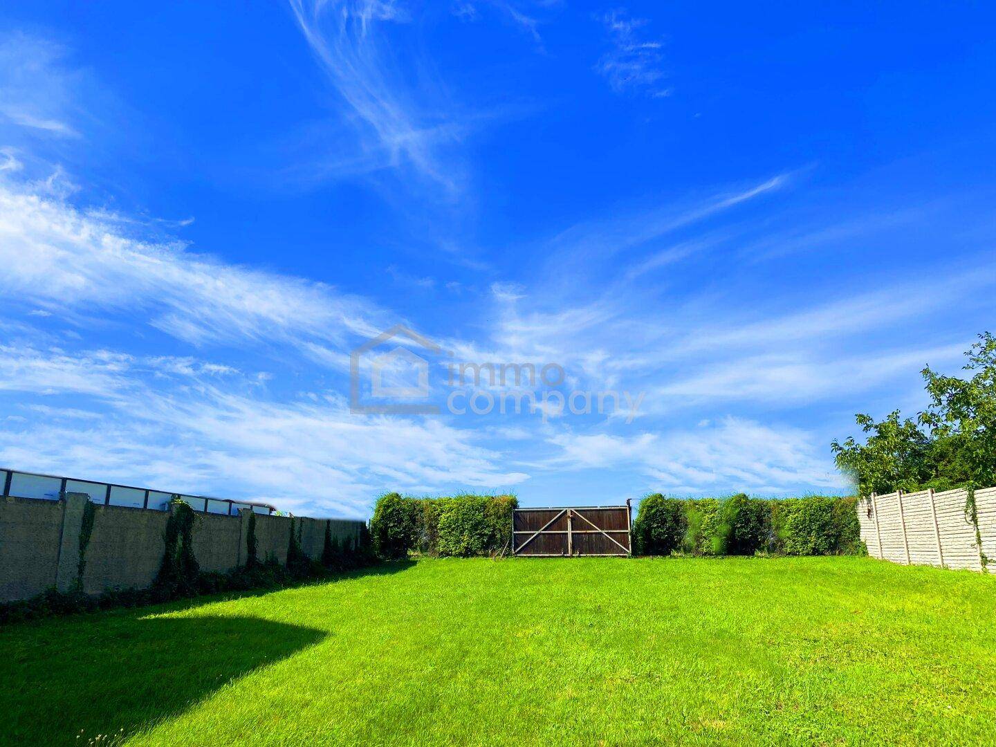 Gepflegter Rasenbereich mit hohen Hecken und einem Holztor unter strahlend blauem Himmel.