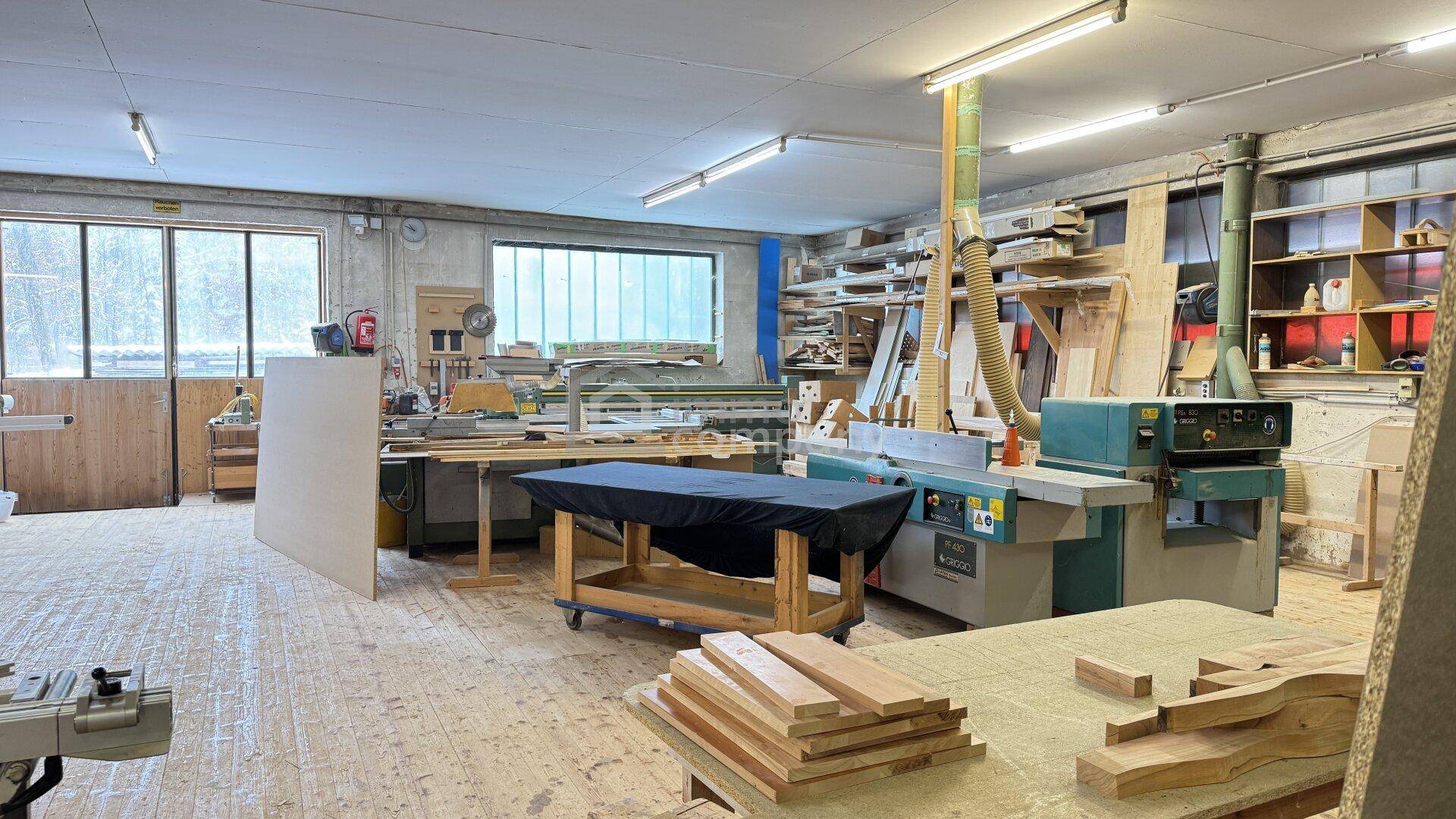 Geräumige Holzwerkstatt mit verschiedenen Maschinen, Werkbänken und gelagertem Holzmaterial.