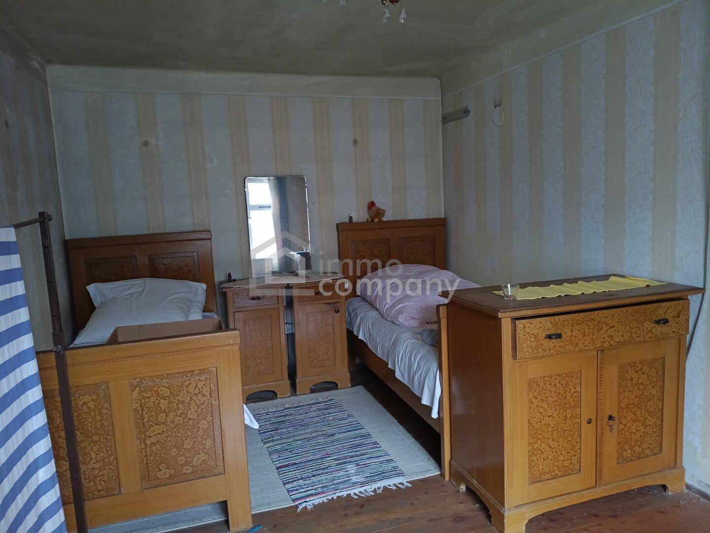Schlafzimmer mit zwei Einzelbetten, Holzmöbeln und gestreifter Tapete.