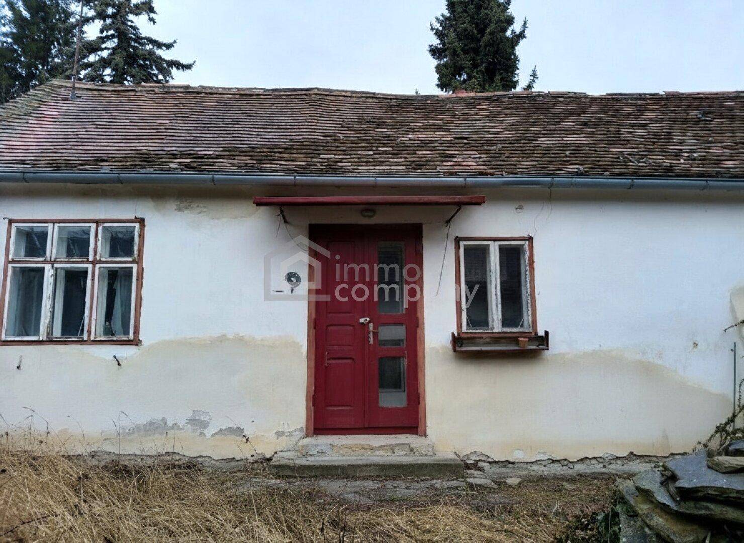 Vorderansicht eines alten Hauses mit roter Eingangstür und verwitterten Fenstern.