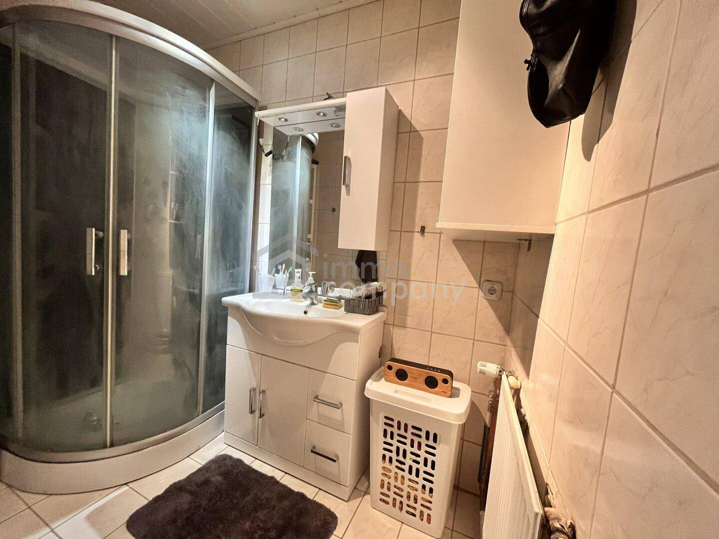 Kleines Badezimmer mit Duschkabine, Waschbeckenunterschrank und hellen Fliesen an Wänden und Boden.