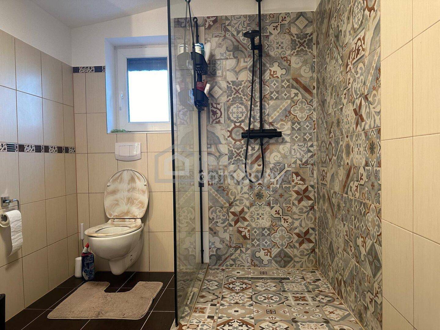 Badezimmer mit WC, großer Dusche und dekorativen Fliesen im Duschbereich.