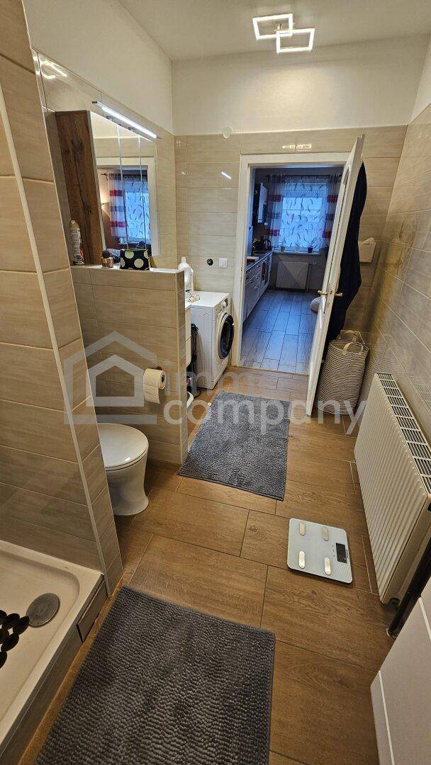 Modernes Badezimmer mit Dusche, WC und Waschmaschine, durch eine Tür zur Küche verbunden.