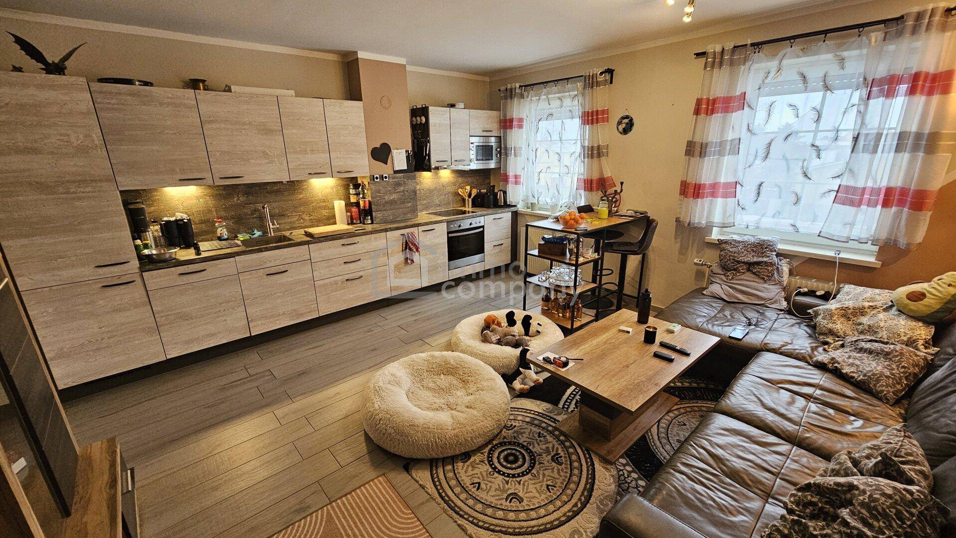 Offener Wohn-Essbereich mit moderner Einbauküche, Ledersofa und Holzboden.