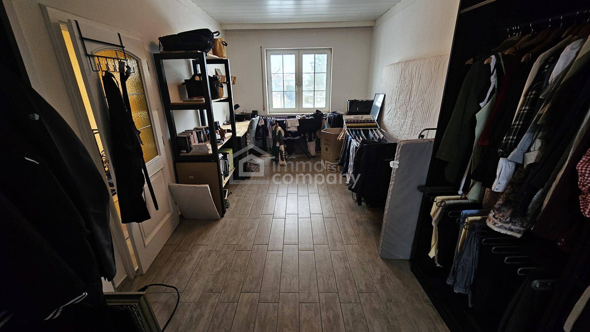 Langer Raum mit Kleiderstangen, Regalen und Fenster, möglicherweise ein Ankleidezimmer.