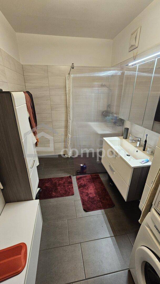 Badezimmer mit Dusche, Doppelwaschbecken und Waschmaschine, gefliestem Boden.