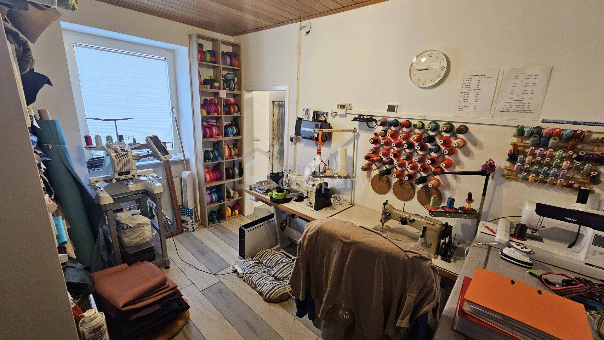 Werkstatt oder Nähzimmer mit Nähmaschinen, Garnrollen und großem Fenster.