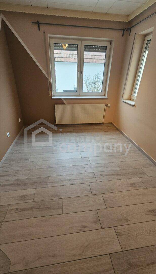 Leeres Zimmer mit Holzboden, Fenster und Heizkörper, bereit zur Einrichtung.