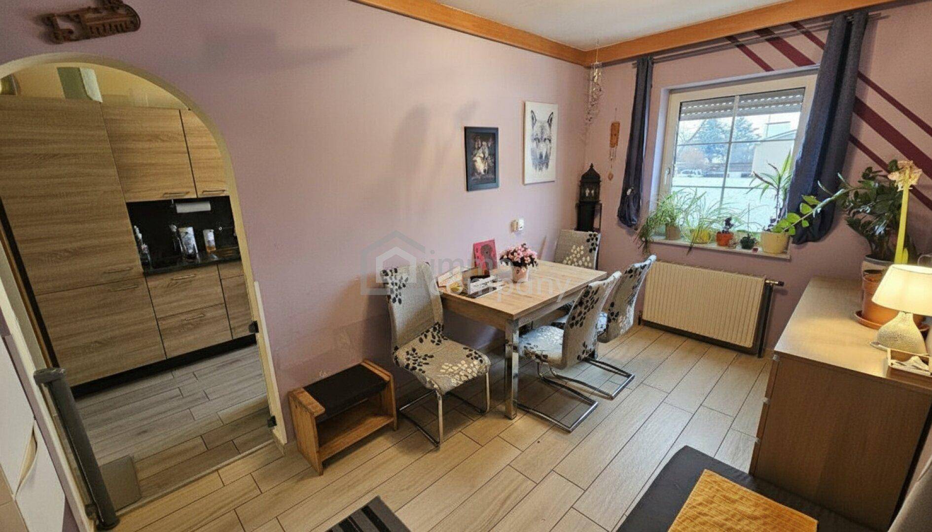Esszimmer mit Holztisch, Stühlen und Zugang zur Küche durch einen Bogen.