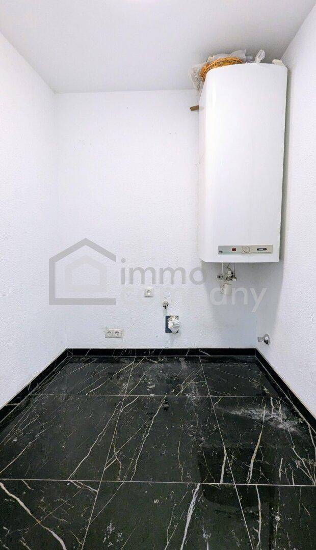 Praktischer Hauswirtschaftsraum mit Warmwasserbereiter und dunklem Fliesenboden.