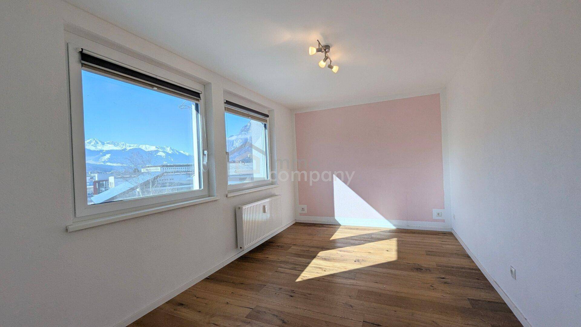Heller Büroraum mit Holzboden, rosa Akzentwand und großen Fenstern mit Bergblick.