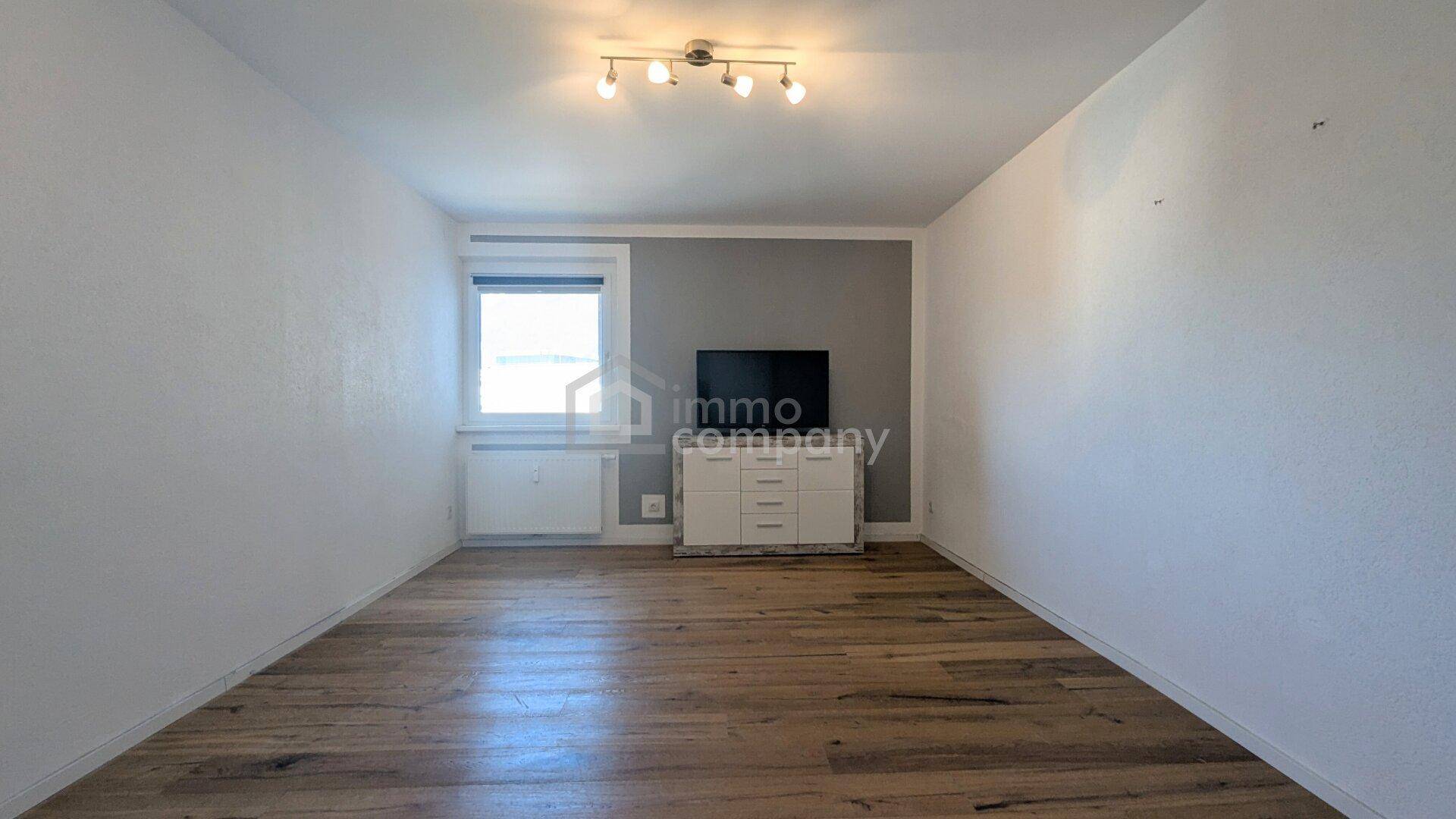 Helles Zimmer mit Holzboden und einem Fenster, ideal als Schlaf- oder Gästezimmer.