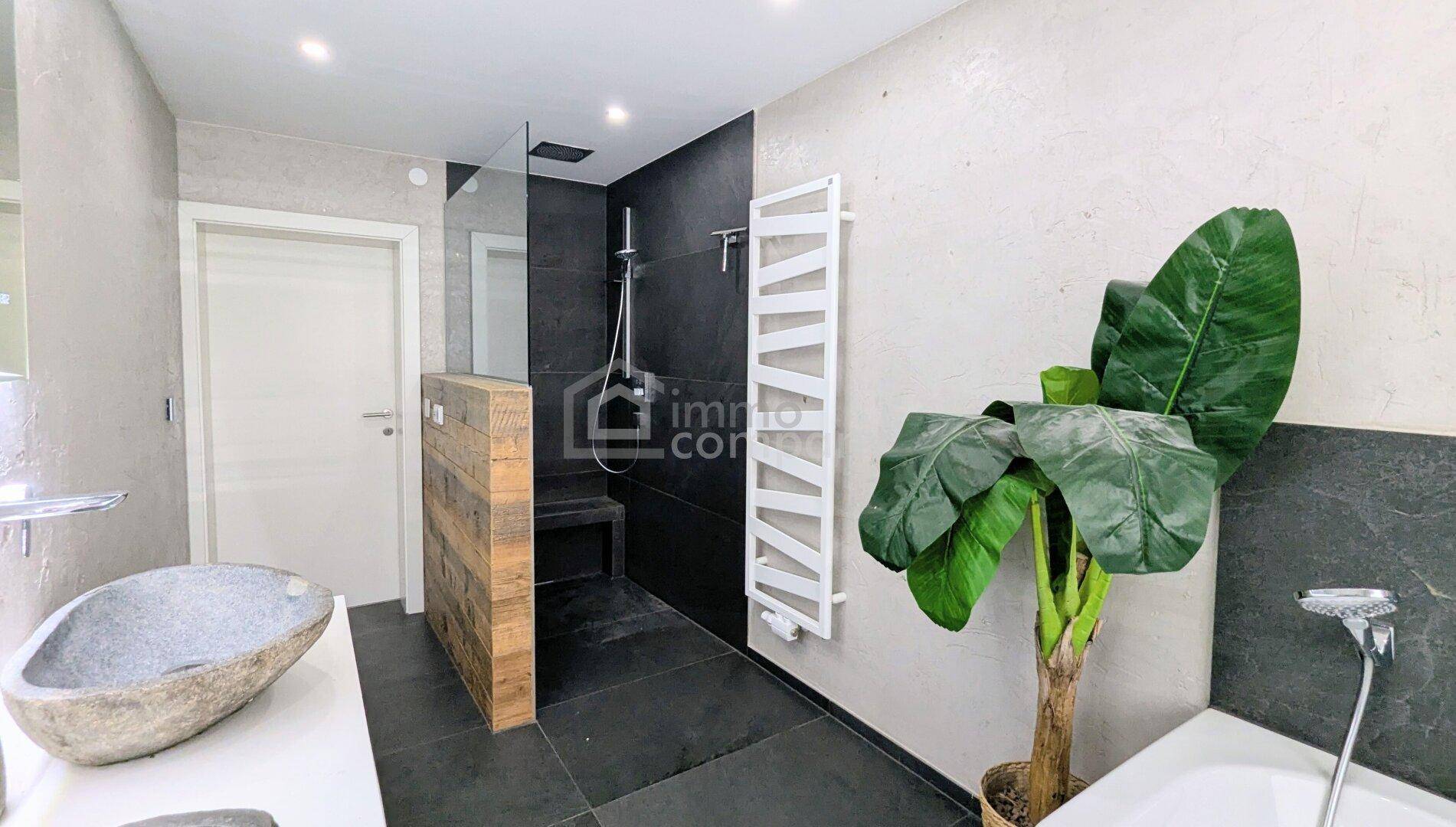 Geräumiges Badezimmer mit moderner begehbarer Dusche, dunklen Fliesen und beheiztem Handtuchhalter.