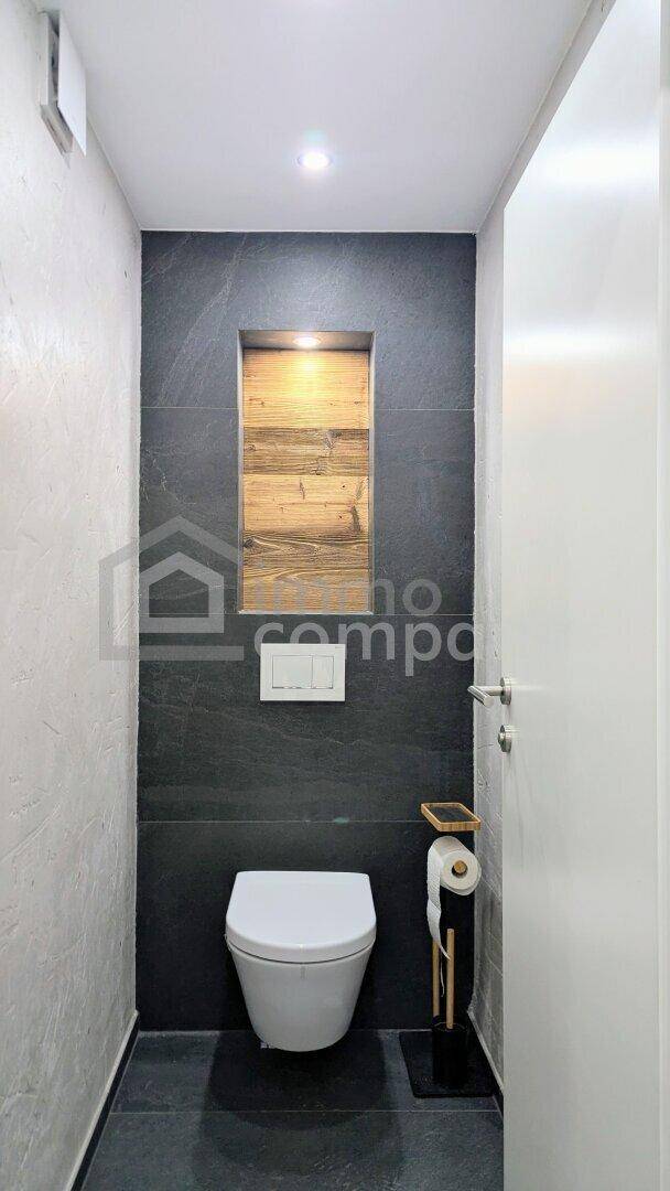 Modernes Gäste-WC mit wandhängender Toilette und dunklen Fliesen an der Wand.