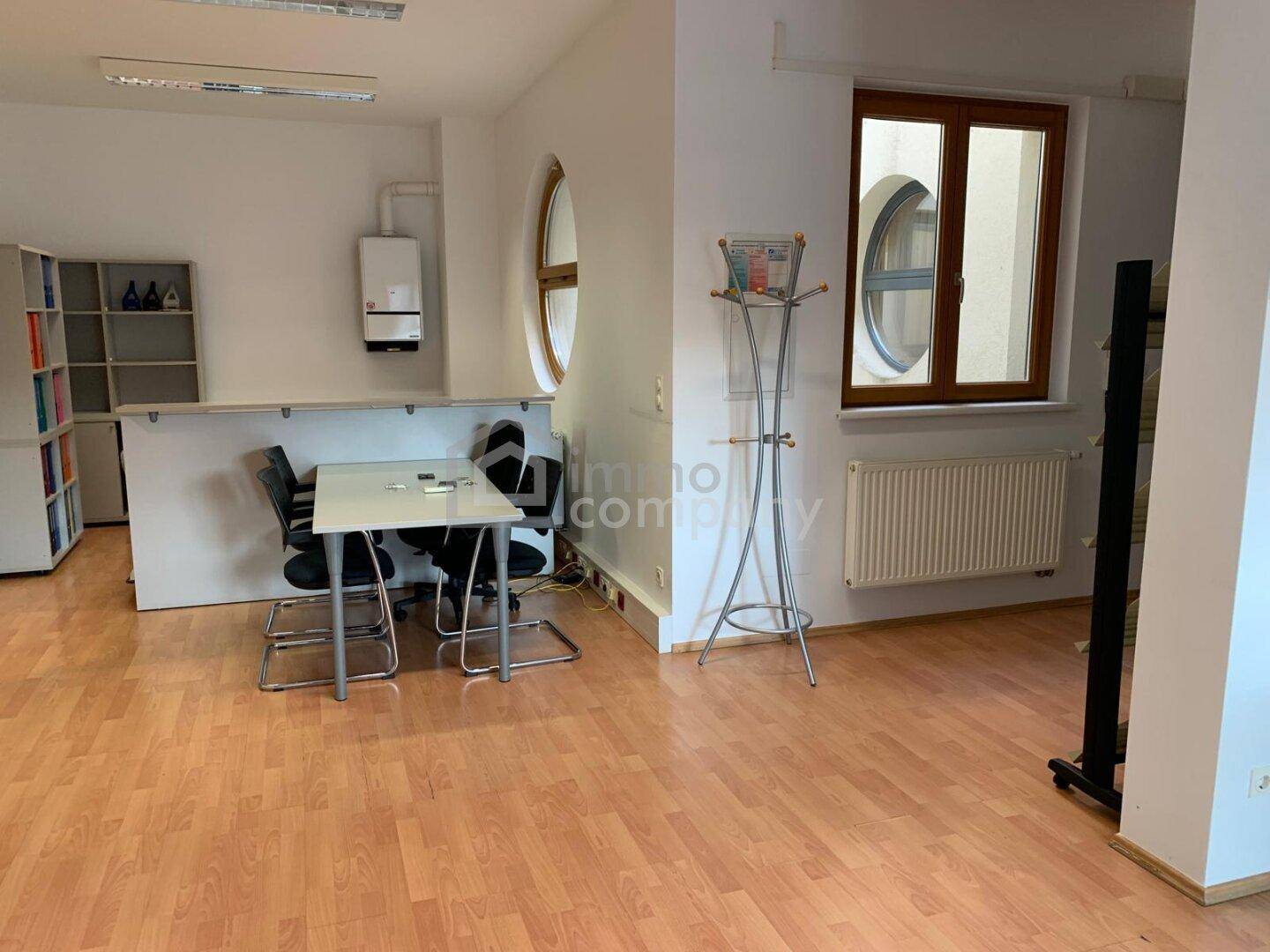 Empfangsbereich oder Wartezimmer mit Heizkörper, runden Fenstern und funktionalen Möbeln.