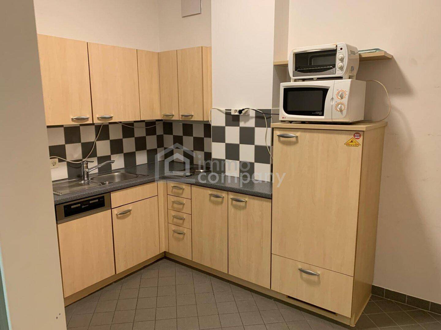 Kompakte Küchenzeile mit Holzschränken, kariertem Fliesenspiegel und integrierten Geräten.