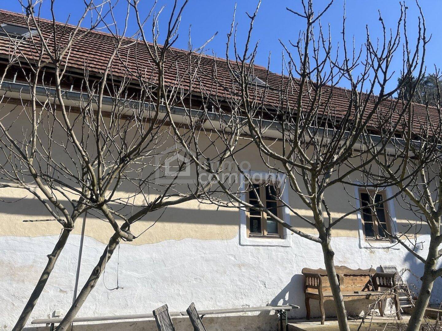 Altes Bauernhaus mit traditionellem Ziegeldach und kahlen Bäumen im Vordergrund.