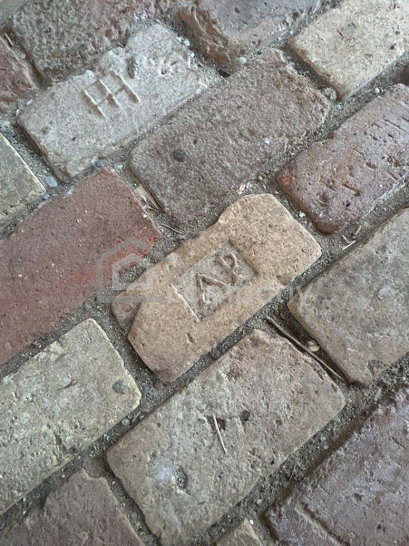 Nahaufnahme eines rustikalen Ziegelbodens mit individuellen Markierungen und Abnutzungsspuren.