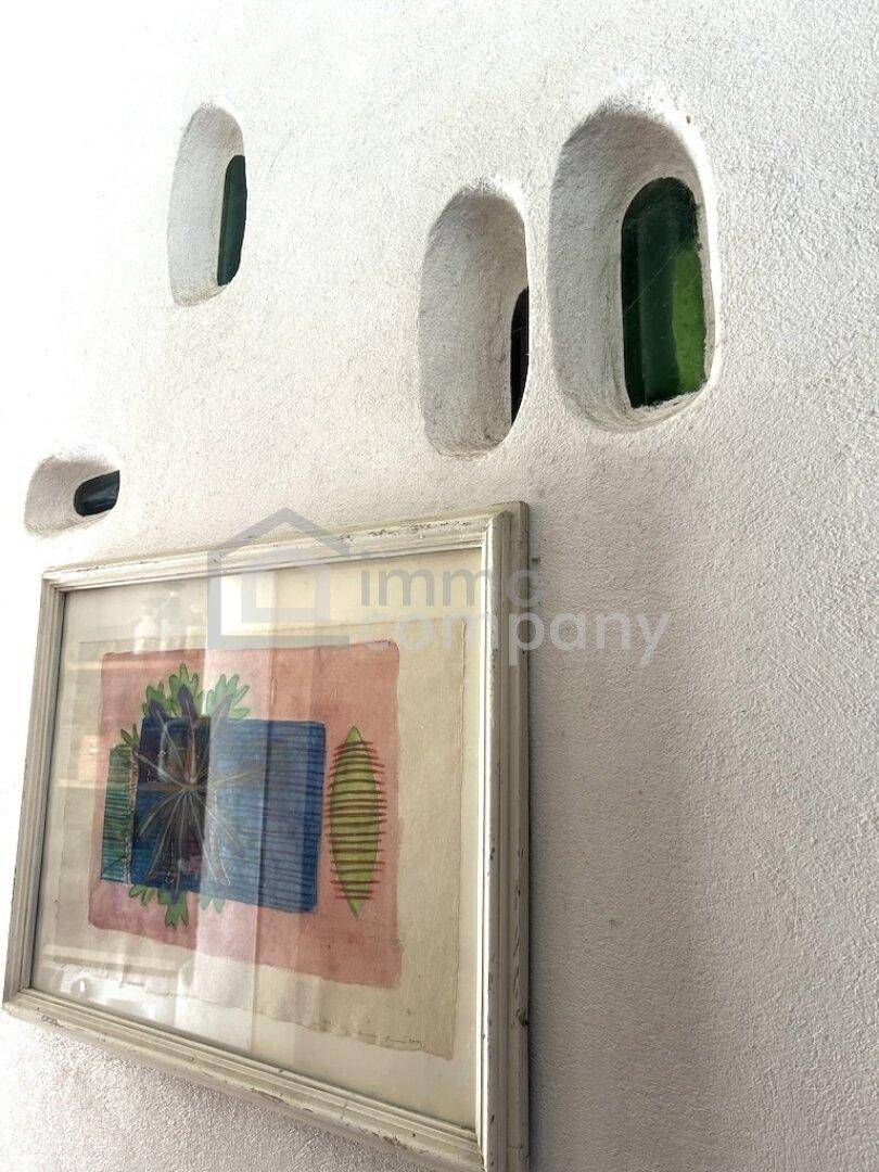 Weiße Wand mit unregelmäßigen Nischen und einem gerahmten Kunstwerk darunter.