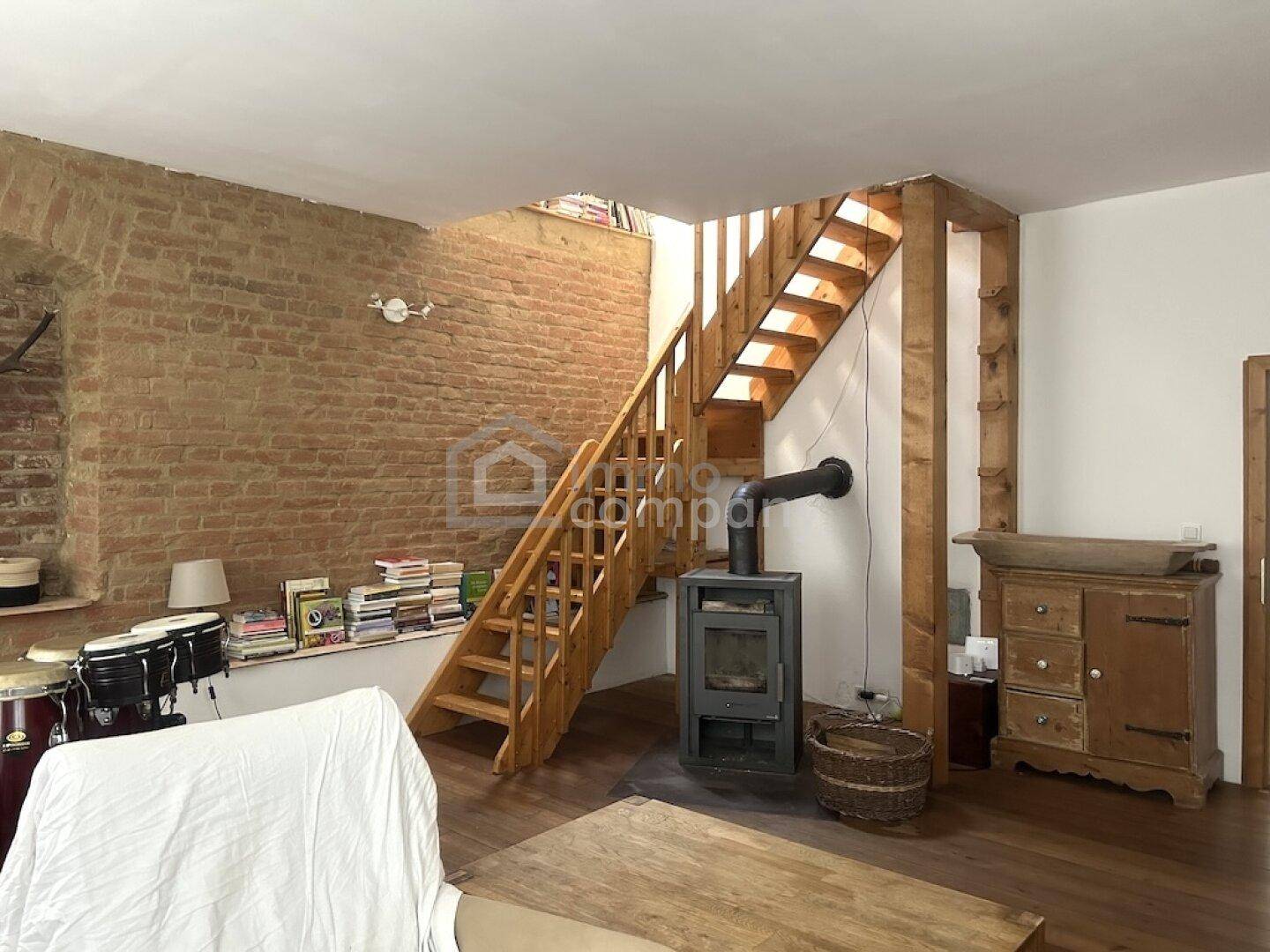 Gemütliches Wohnzimmer mit freiliegender Ziegelwand, Holztreppe und Kaminofen.