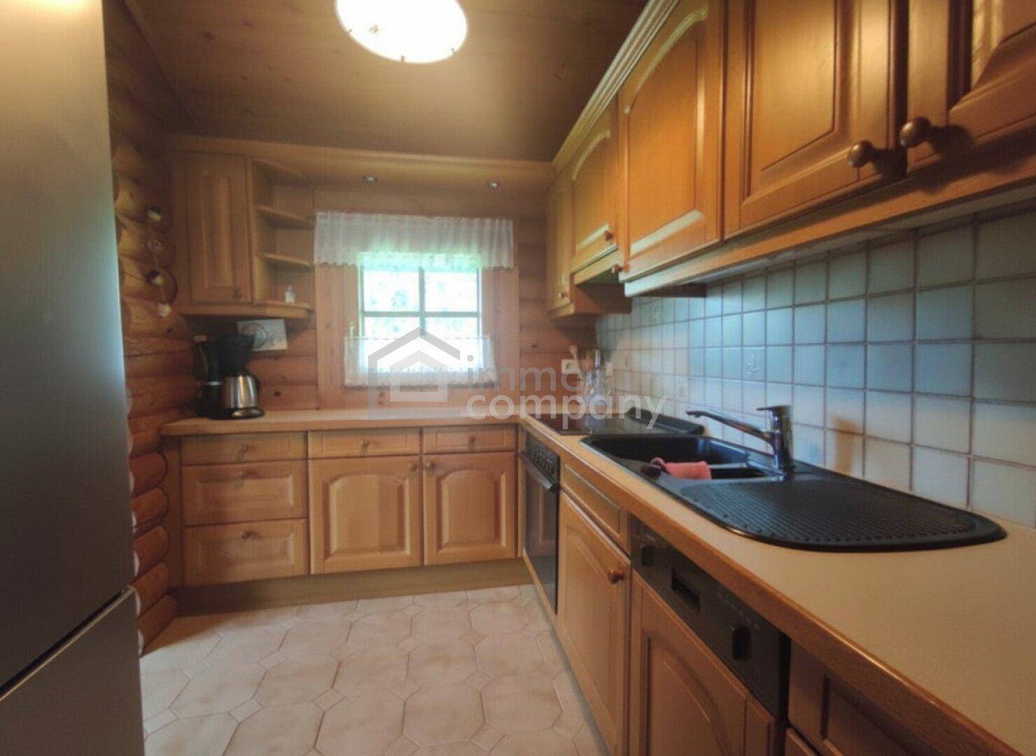 Rustikale Holzküche mit Einbauschränken, Fliesenboden und Fenster mit Blick ins Grüne.