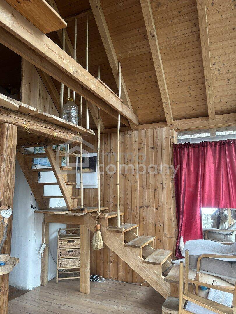 Rustikaler Innenraum mit Holzverkleidung, offener Holztreppe und sichtbaren Holzbalken.