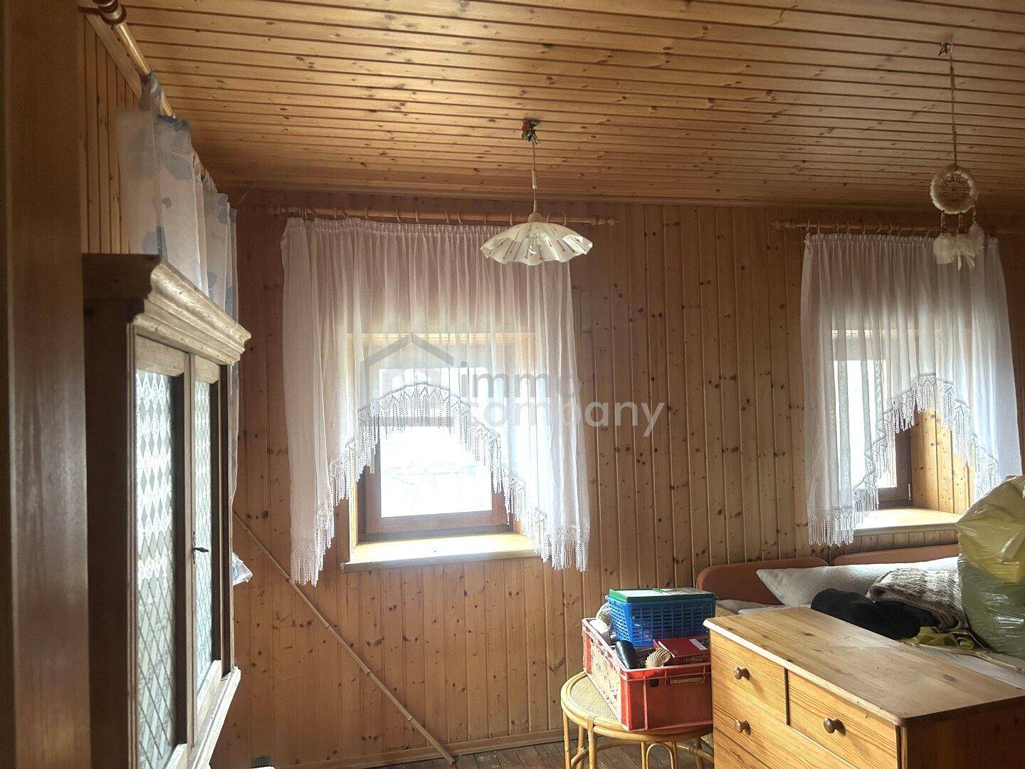 Gemütliches Schlafzimmer mit Holzvertäfelung und zwei Fenstern, die viel Tageslicht hereinlassen.