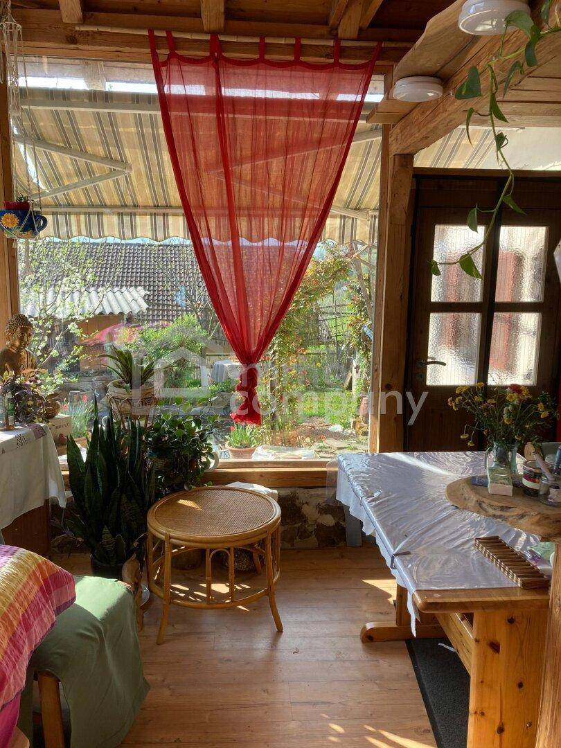 Heller Wintergarten mit großen Fenstern, Pflanzen und gemütlicher Sitzecke, ideal zum Entspannen.