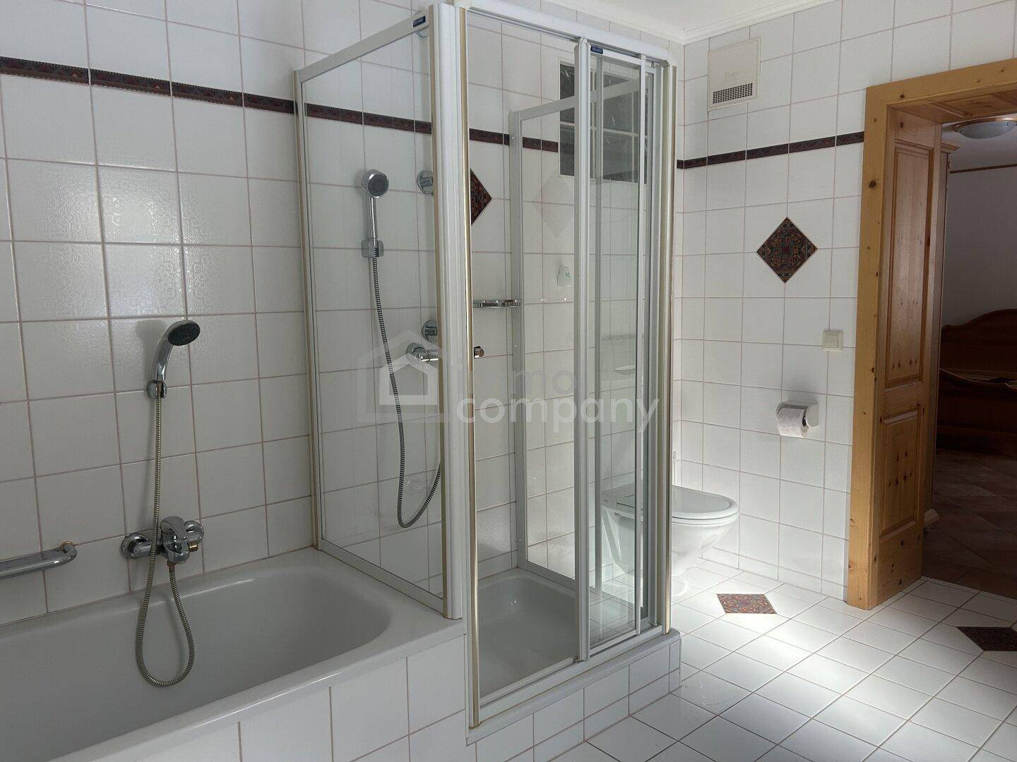 Funktionales Badezimmer mit weißen Fliesen, Badewanne, Duschkabine und Haltegriffen für zusätzliche Sicherheit.
