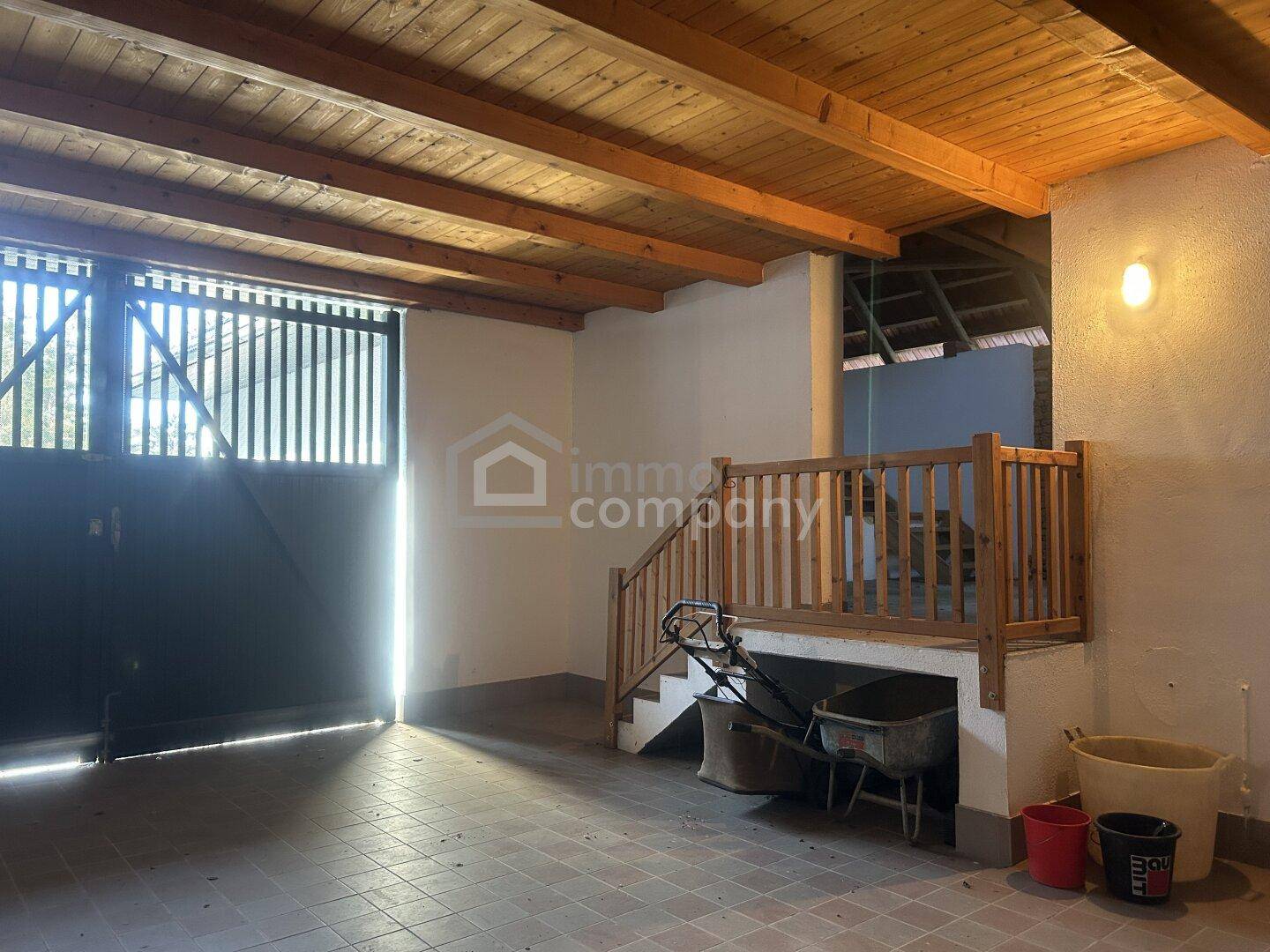 Geräumige Garage oder Abstellraum mit Holztor, Betonboden und sichtbaren Deckenbalken, inklusive kleiner Holztreppe.