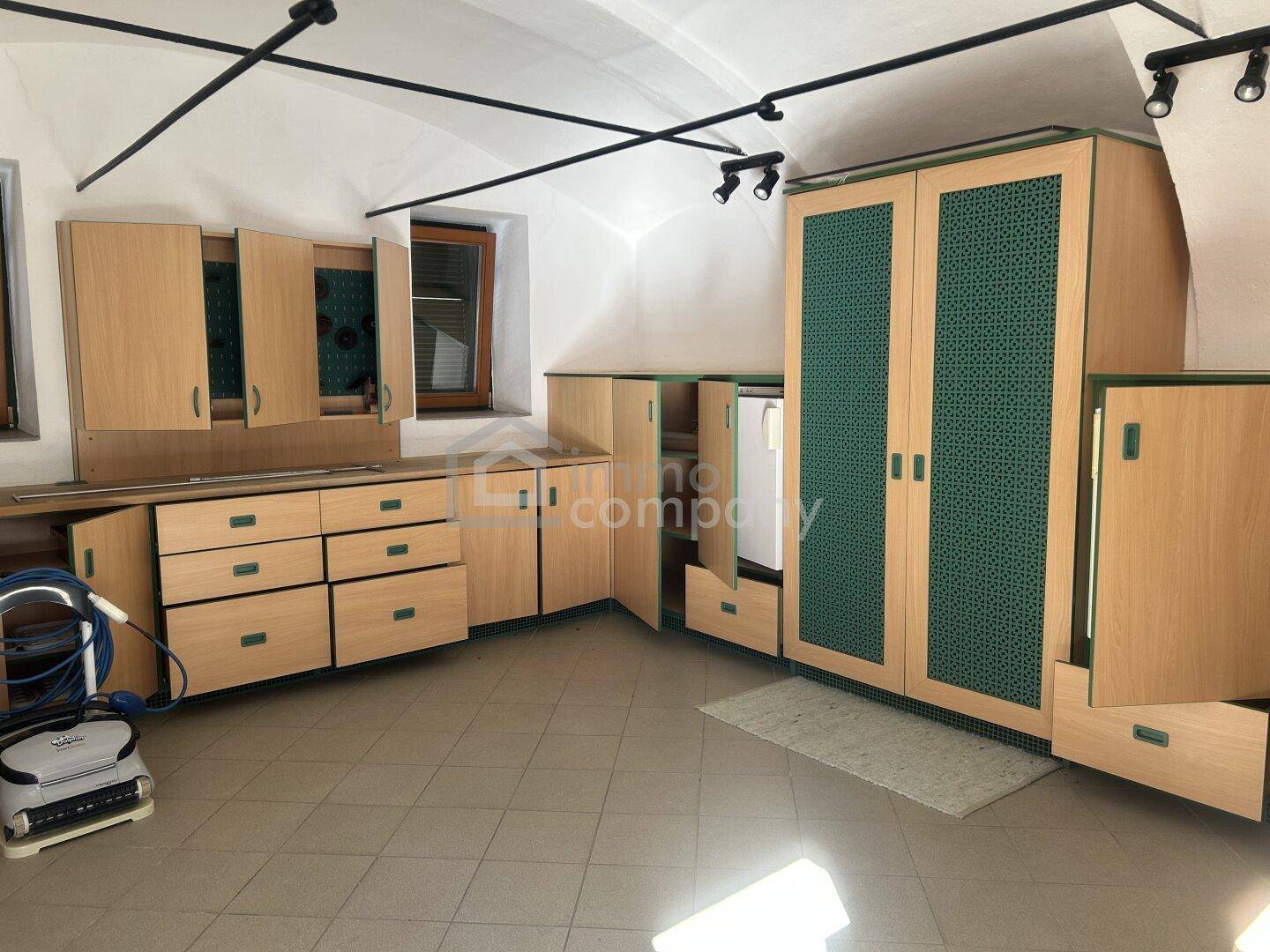Heller Werkstattraum mit maßgefertigten Holzschränken, Werkbank und Fliesenboden unter einem schrägen Dach.