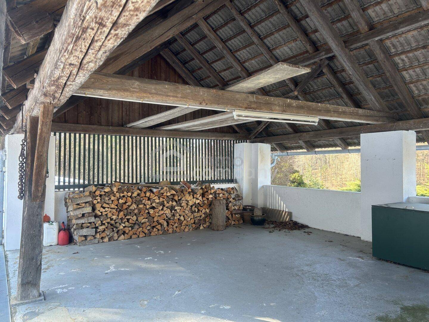 Überdachter Außenbereich mit großem Holzstapel und sichtbarer Holzkonstruktion, ideal als Lager oder Unterstand.
